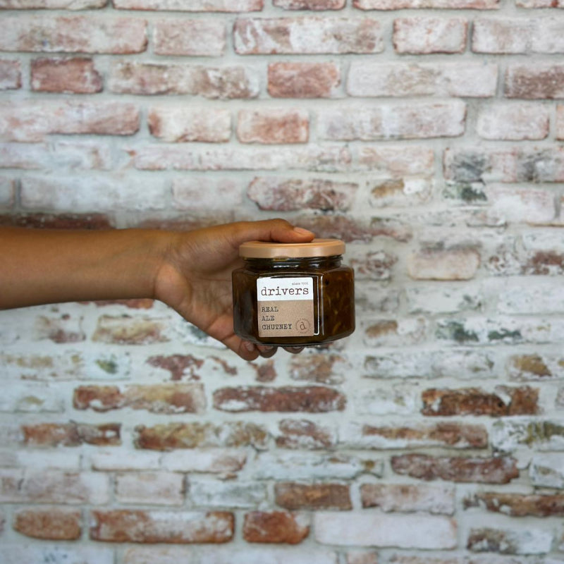 Hand holding Drivers Real Ale Chutney against a brick wall.