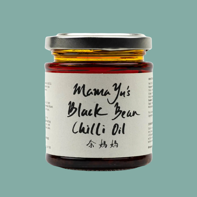 A glass jar of Mama Yu's Black Bean Chilli Oil with a white label and silver lid, set against a solid teal background.