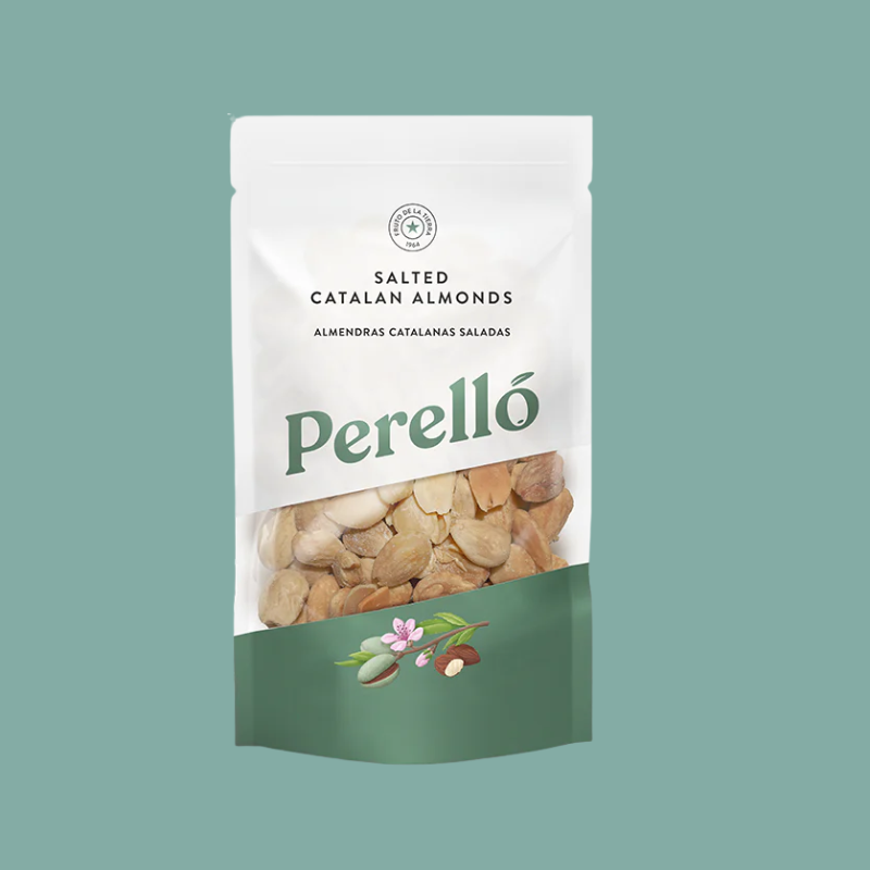 A stand-up pouch of Perelló Salted Catalan Almonds on a solid sage green background. The packaging is white on the top half with dark green text, and has a clear window showing sliced almonds inside, with a dark green bottom section decorated with almond illustrations.