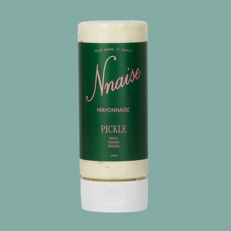 A squeeze bottle of Nnaise Mayonnaise Pickle, featuring a dark green label with pink and white text, filled with creamy off-white mayonnaise, and capped with a white screw-top lid, set against a solid teal background.