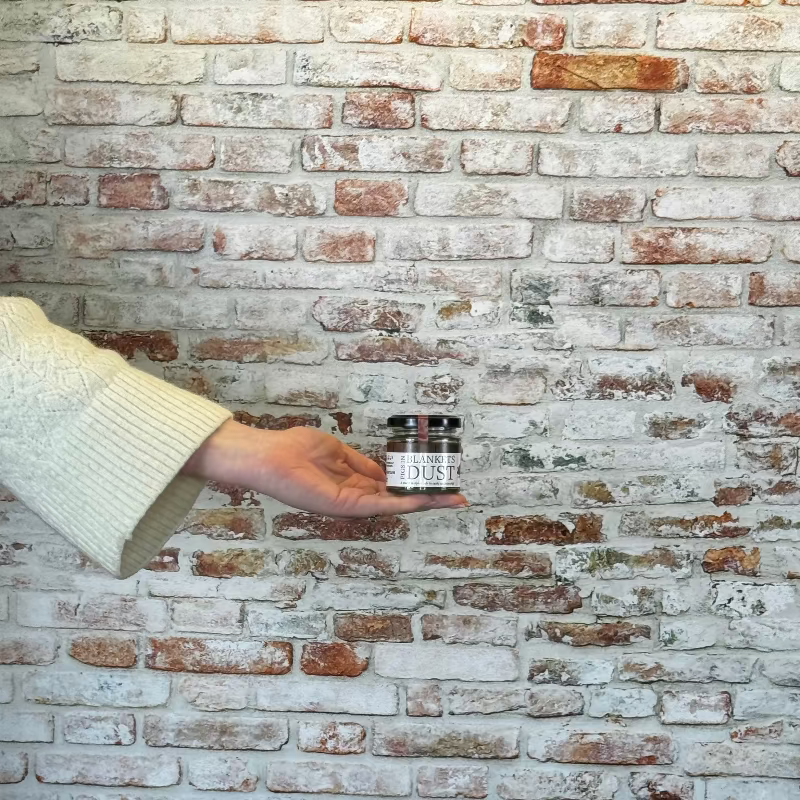 Person holding a small container against a brick wall