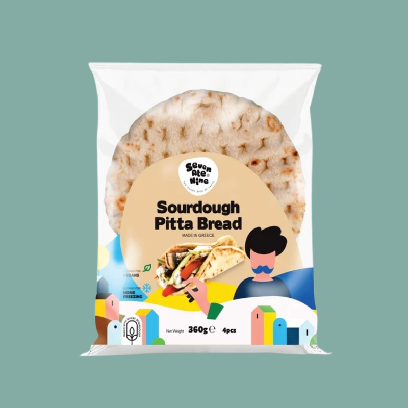 A package of Seven Ate Nine Sourdough Pitta Bread, featuring a large photo of a round flatbread on a white and beige bag with colorful cartoon illustrations at the bottom, set against a solid sage green background.