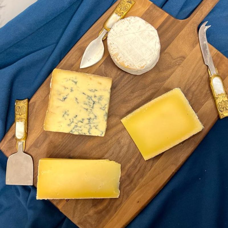 Cheese board full of artisanal and british famrhosue cheese, Montgoemrys cheddar, Kern cheese, Colston bassett stilton and winslade cheese  with three cheese knives