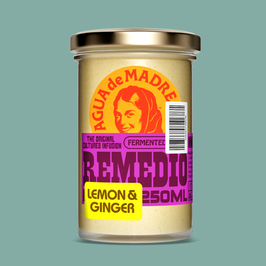 A 250ml glass jar of Agua de Madre Remedio Lemon & Ginger, featuring a gold metal lid and a colorful label with orange, purple, and yellow text, set against a solid teal background.