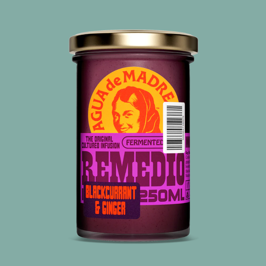 A 250ml glass jar of Agua de Madre Remedio Blackcurrant & Ginger, featuring a gold lid and a colorful label with a retro-style woman's face, set against a solid teal background.