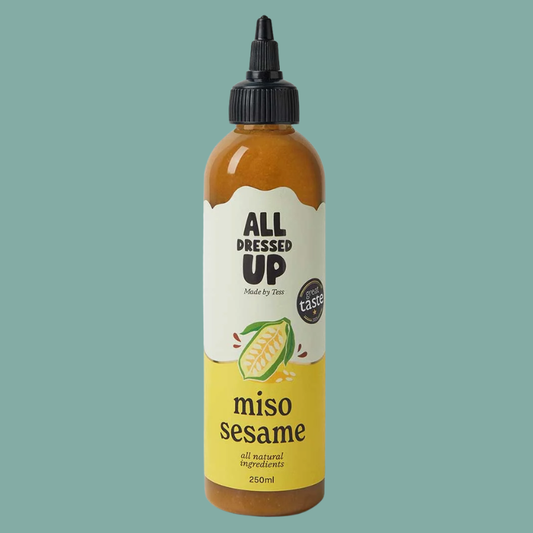 A 250ml squeeze bottle of All Dressed Up Miso Sesame dressing, featuring a black cap and a label with a white top half and a yellow bottom half, set against a solid teal background.