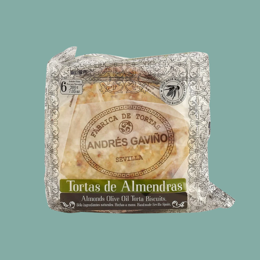 A packaged block of Andrés Gaviño Tortas de Almendras (Almonds Olive Oil Torta Biscuits) from Fabrica de Tortas in Seville, Spain, wrapped in clear plastic with a decorative silver patterned border and a central label, set against a solid teal background.