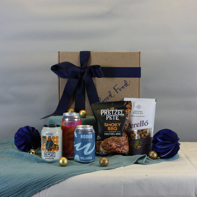 Gift basket with snacks and drinks on a table against a plain background