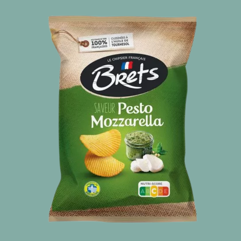 A bag of Brets Pesto Mozzarella potato chips on a solid teal background. The packaging features a green lower half with illustrations of yellow chips, garlic, and a jar of green pesto, and a brown burlap-textured top half with the Brets logo.