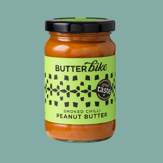 A jar of Butterbike Smoked Chilli Peanut Butter on a solid teal background. The product is in a clear glass jar showing the orange-brown peanut butter inside, with a bright lime green label and a black lid.