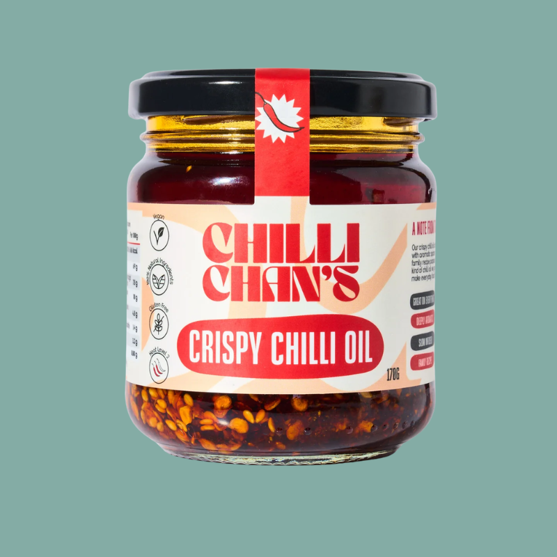 A glass jar of Chilli Chan's Crispy Chilli Oil with a black lid and a red and white label, set against a solid teal-green background.