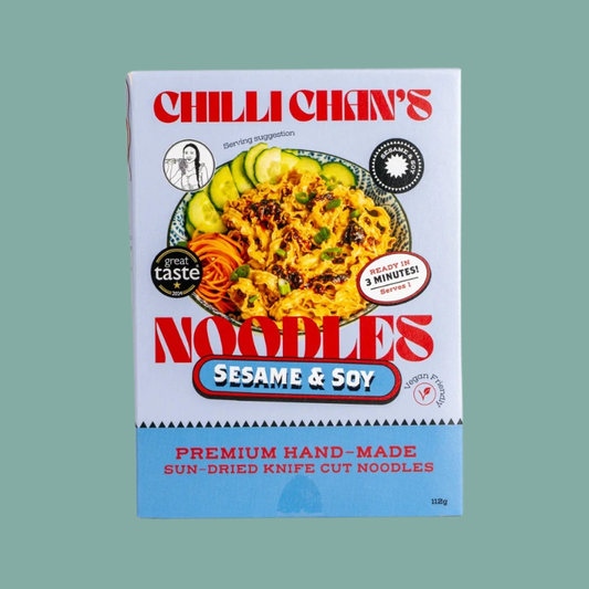 A package of Chilli Chan's Sesame & Soy Noodles on a solid sage green background. The packaging is white on the top half with a colorful food photo of the prepared noodles, and light blue on the bottom half with red text.