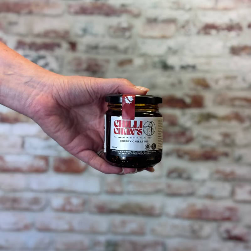 Hand holding a jar of Chilli Chan's crispy Chilli oil against a brick wall background