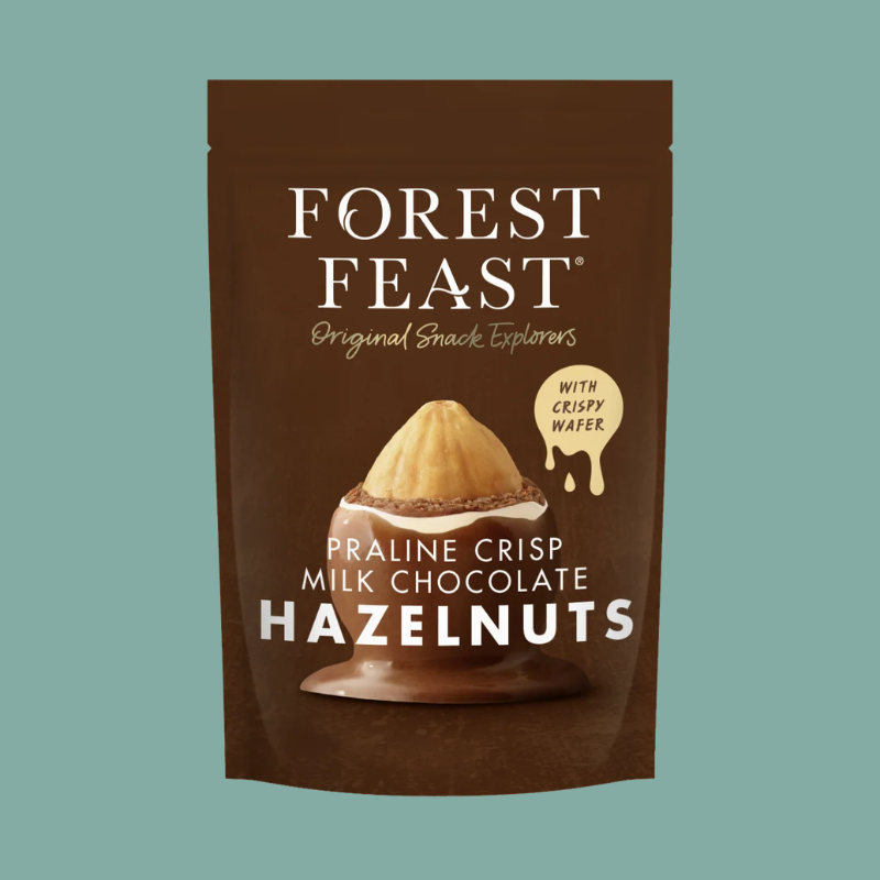 Forest Feast Praline Crisp Milk Chocolate Hazelnuts in a brown stand-up pouch with white text and a chocolate-hazelnut illustration, shown on a muted teal background.
