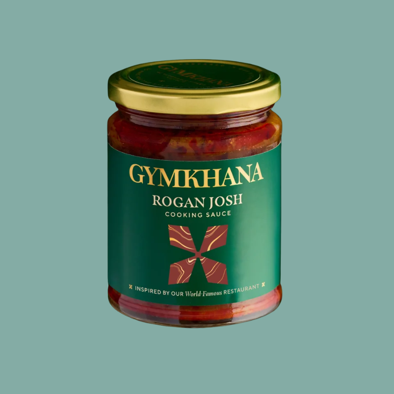 A glass jar of GYMKHANA Rogan Josh cooking sauce with a gold lid and a dark green label, centered on a solid sage green background.