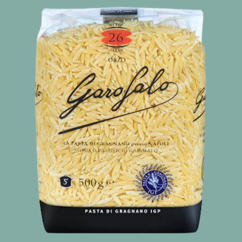 A 500g bag of Garofalo Grano Orzo pasta, showing the yellow grains inside a clear bag with a black base and brand logo, set against a solid sage green background.