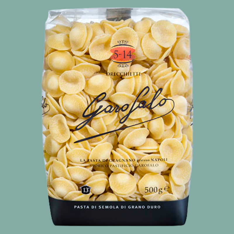 A 500g bag of Garofalo durum wheat pasta orecchiette on a solid sage green background. The packaging is clear, showing the pale yellow pasta inside, with a black base and a red circular logo.