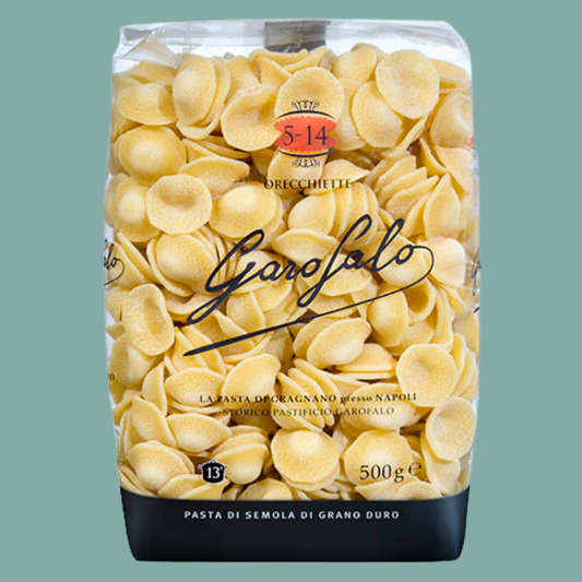 A 500g bag of Garofalo durum wheat pasta orecchiette on a solid sage green background. The packaging is clear, showing the pale yellow pasta inside, with a black base and a red circular logo.