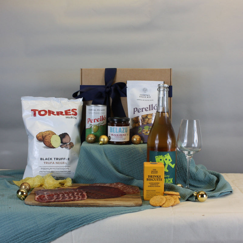 Table with snacks, drinks, and a bottle of wine on a white surface.