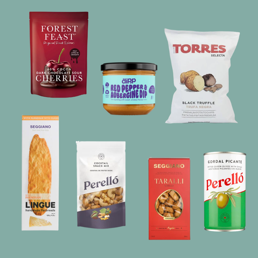 A collage of seven packaged food products arranged on a flat muted green background: Forest Feast sour cherries pouch, a jar of Red Pepper & Aubergine Dip, a bag of Torres Selecta black truffle fries, a box of Seggiano Lingue, a bag of Perelló cocktail snack mix, a red bag of Seggiano Taralli, and a green can of Perelló Cordon Picante.