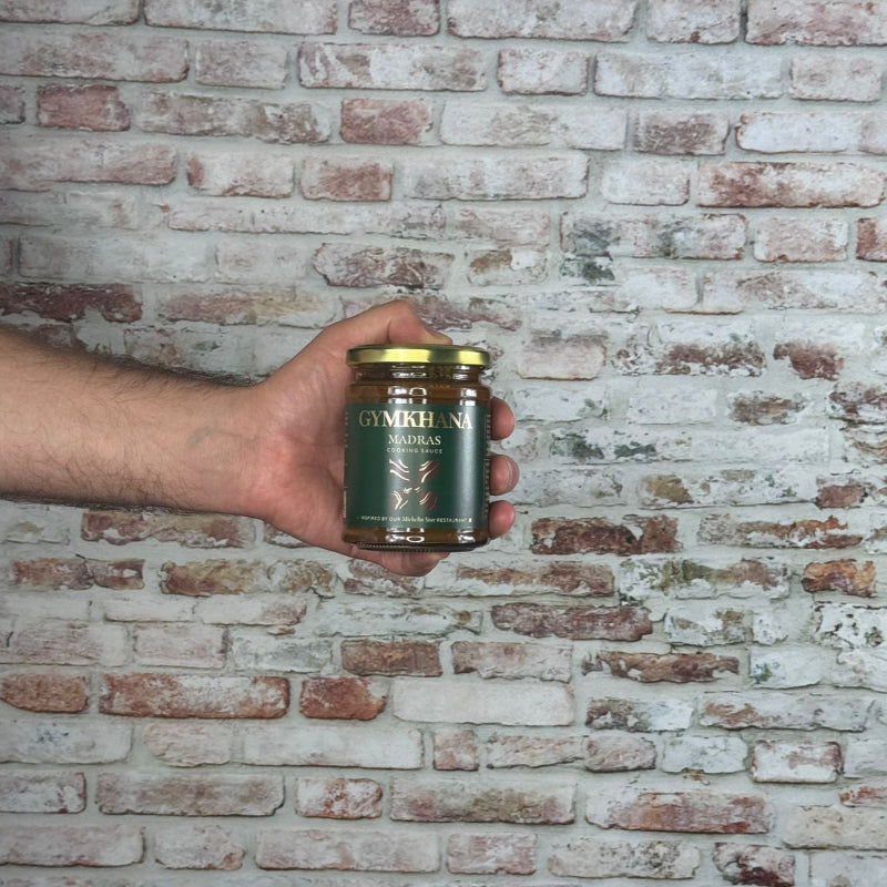 Hand holding a jar of Gymkhana Madras sauce against a brick wall.