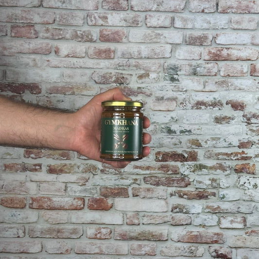 Hand holding a jar of Gymkhana Madras sauce against a brick wall.