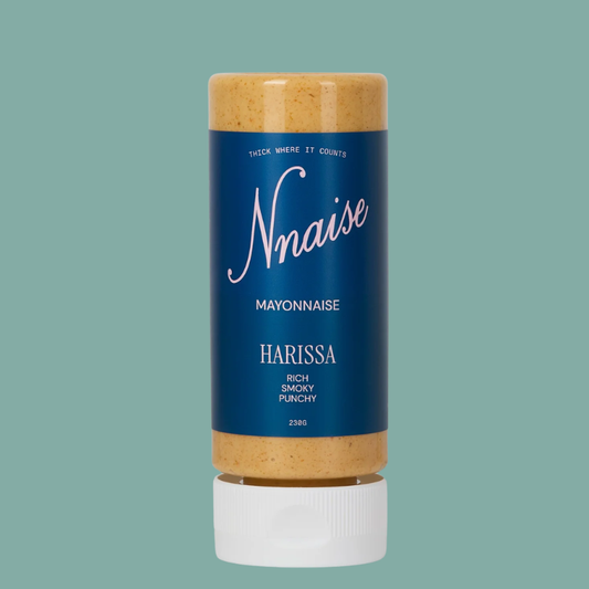 A squeeze bottle of Nnaise Harissa Mayonnaise, featuring a dark blue label with white text and a white cap, filled with orange-brown harissa paste, set against a solid teal background.