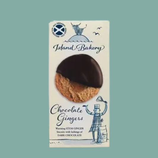 A package of Island Bakery Chocolate Gingers on a solid teal background. The packaging is off-white with blue illustrations and text, featuring a photo of a ginger biscuit half-dipped in dark chocolate.