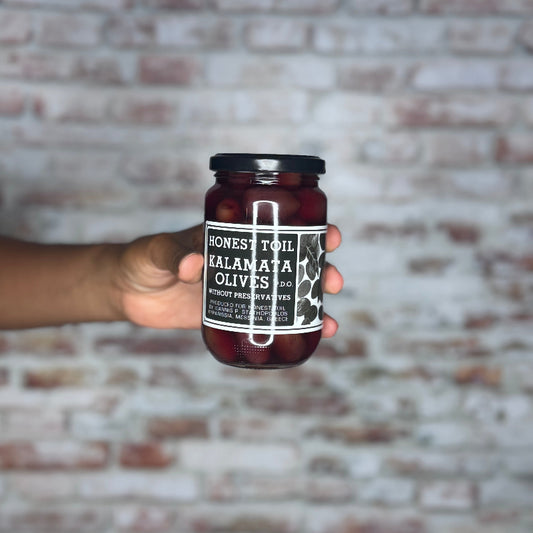 Hand holding a jar of olives against a brick wall background