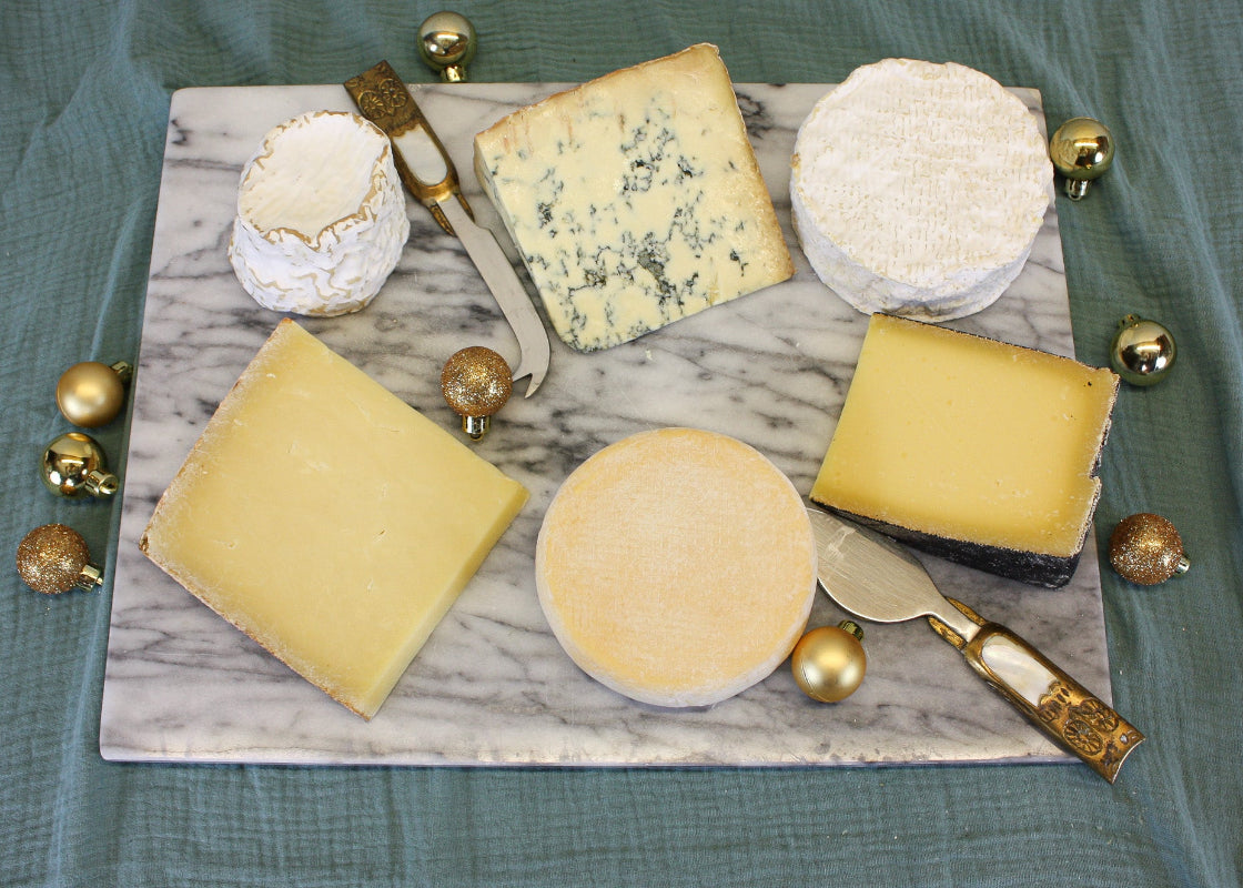 Assorted cheeses on a marble board with gold accents on a green fabric background