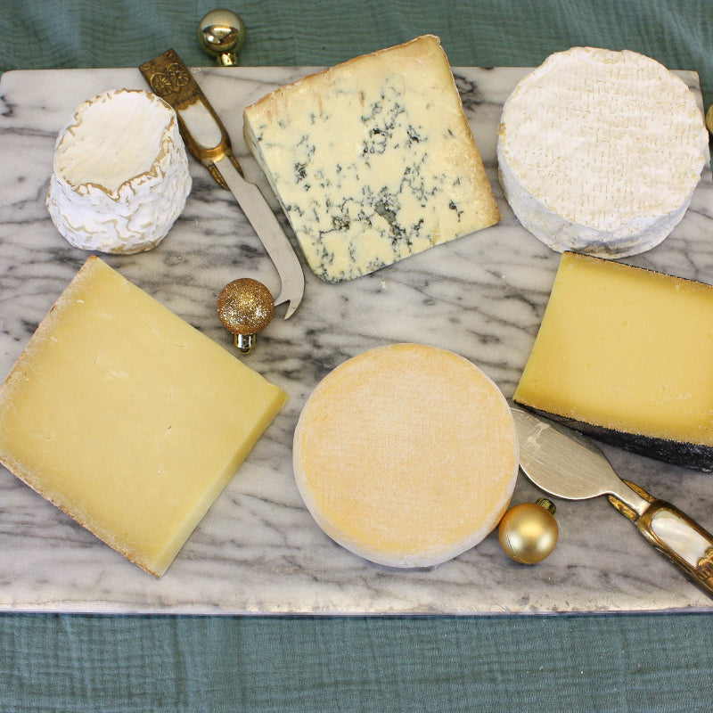 Assorted cheeses on a marble board with gold accents on a green fabric background
