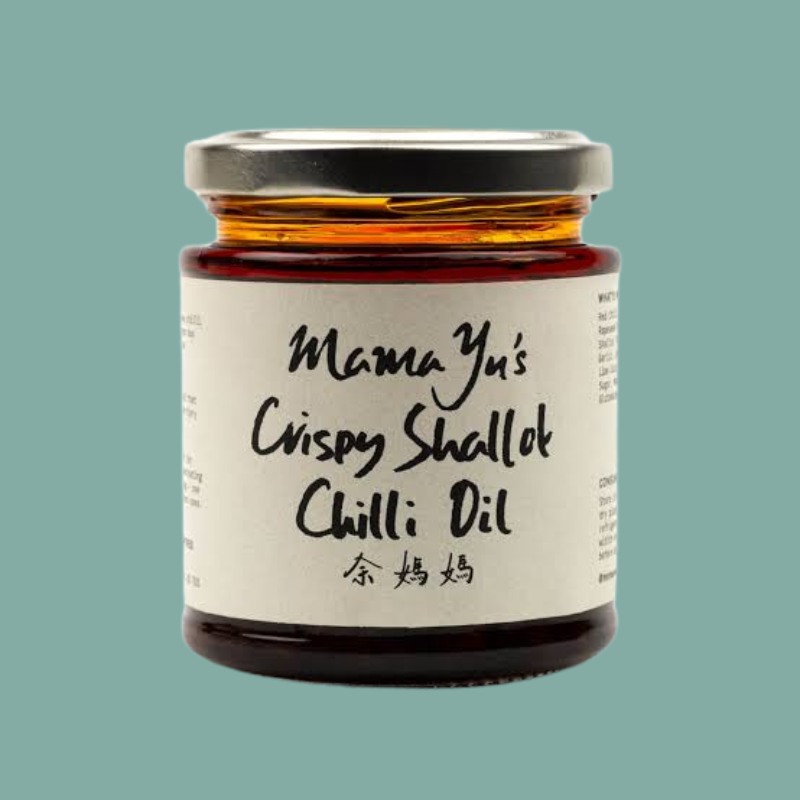 A glass jar of Mama Yu's Crispy Shallot Chilli Oil with a white label and a silver lid, set against a solid teal background.