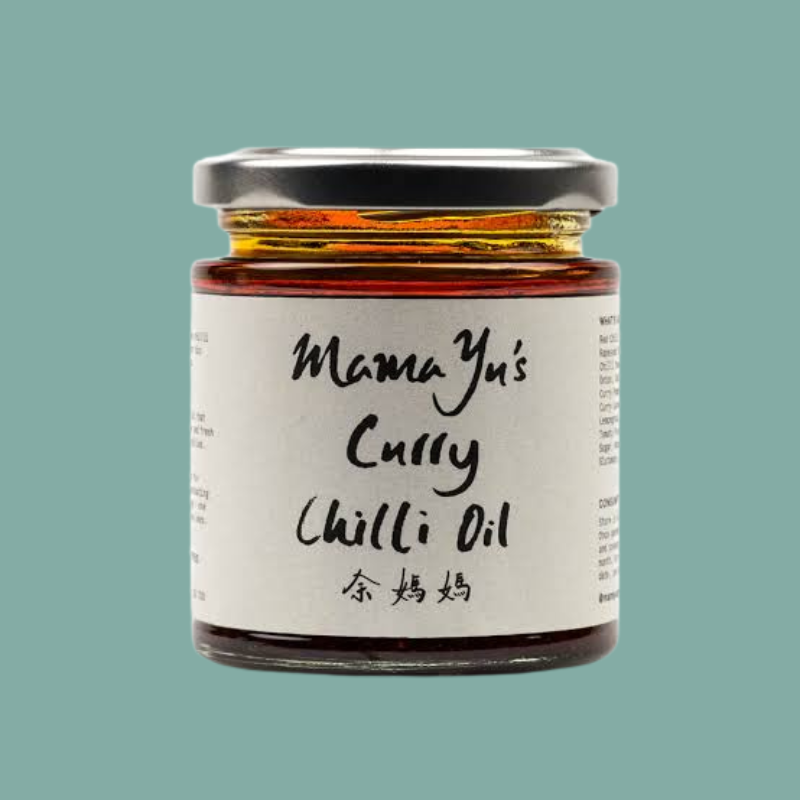 A glass jar of Mama Yu's Curry Chilli Oil with a white label and black lid, centered on a solid teal-green background.