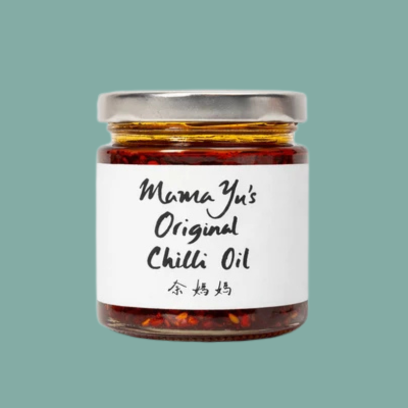 A glass jar of Mama Yu's Original Chilli Oil with a white label and silver lid, centered on a solid teal background.