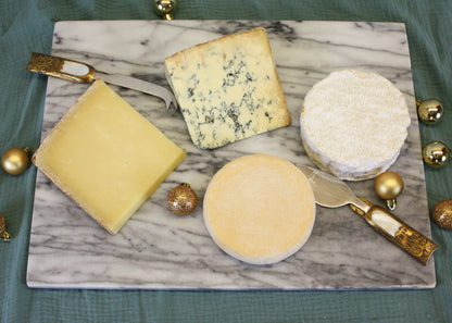 Assorted cheeses on a marble board with decorative gold balls on a green fabric background