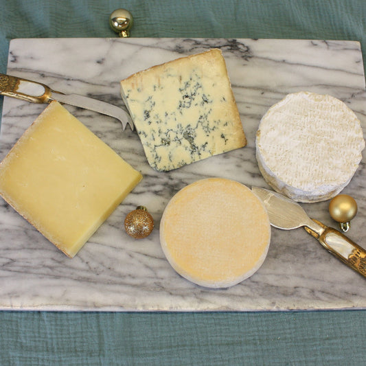 Assorted cheeses on a marble board with gold accents on a green fabric background