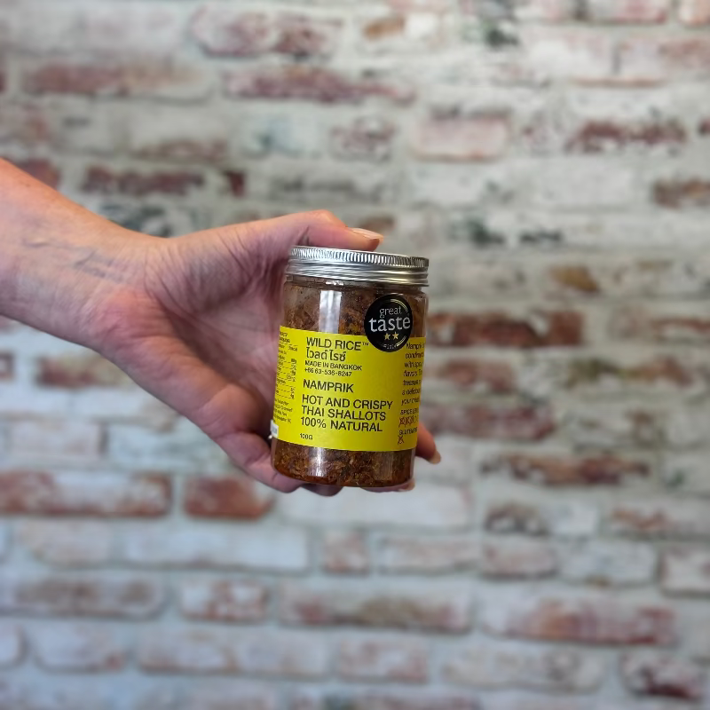 Hand holding a jar of Namprik against a brick wall.