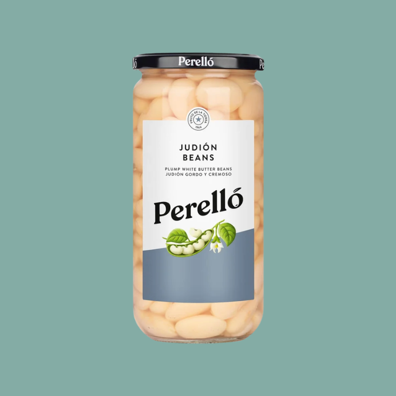 A glass jar of Perelló Judión Beans (pump white butter beans) with a black lid and a white and gray label, centered on a solid teal background.