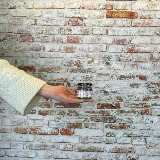 Person holding a small container against a brick wall
