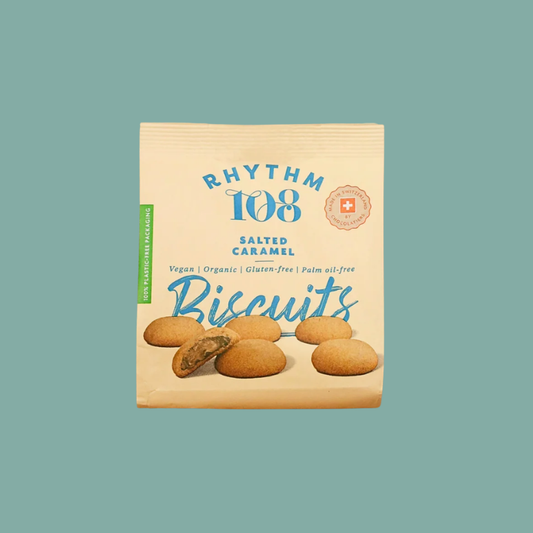 A package of Rhythm 108 Salted Caramel Biscuits on a solid teal background. The packaging is a light beige paper bag with blue text and illustrations of the golden-brown biscuits.