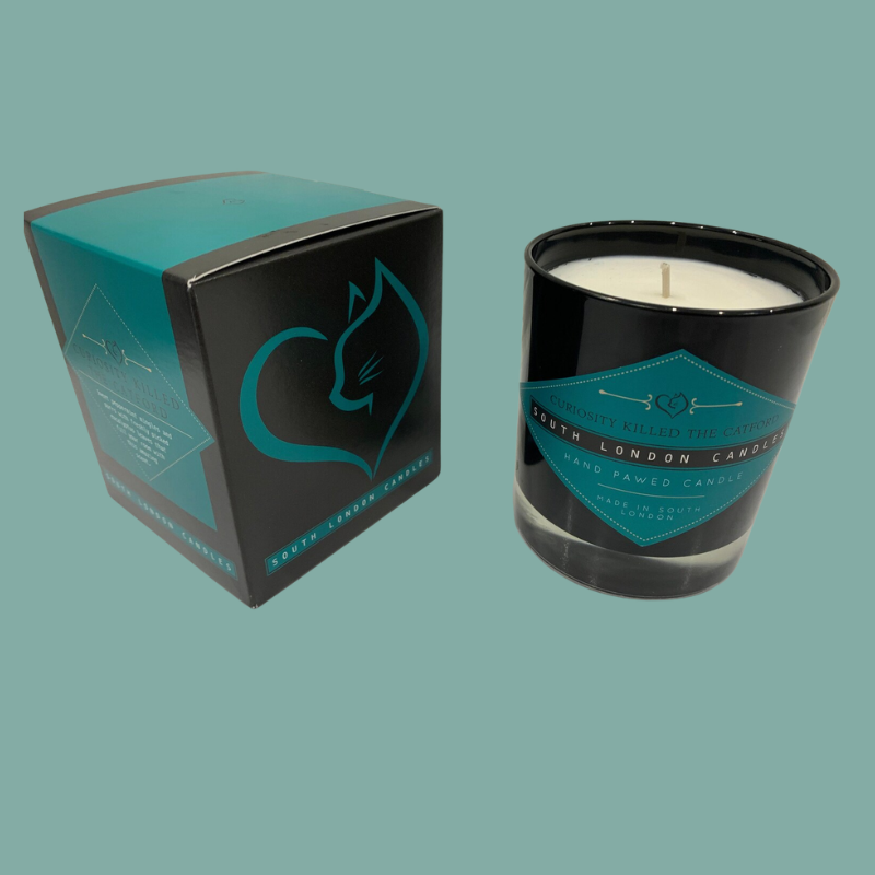 A black glass jar candle with white wax and a teal label, shown next to its matching black and teal box on a solid teal background. 