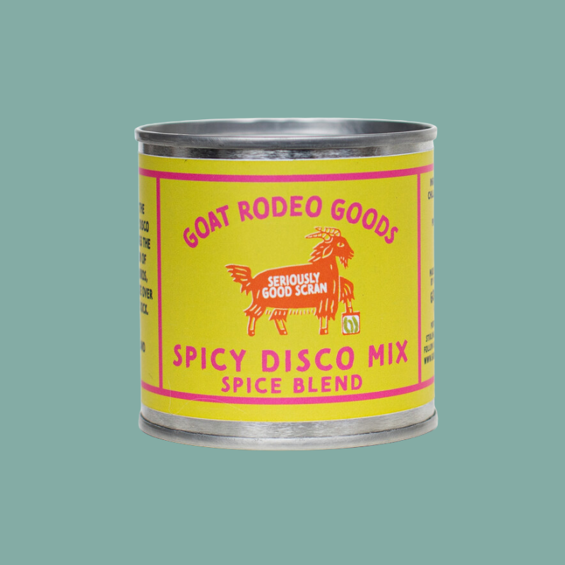 A metal tin of Goat Rodeo Goods Spicy Disco Mix Spice Blend, featuring a bright yellow label with pink text and a red goat illustration, set against a solid teal background.