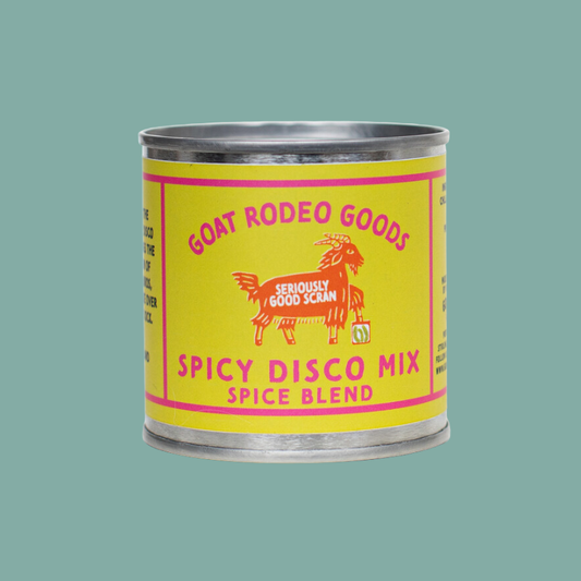 A metal tin of Goat Rodeo Goods Spicy Disco Mix Spice Blend, featuring a bright yellow label with pink text and a red goat illustration, set against a solid teal background.