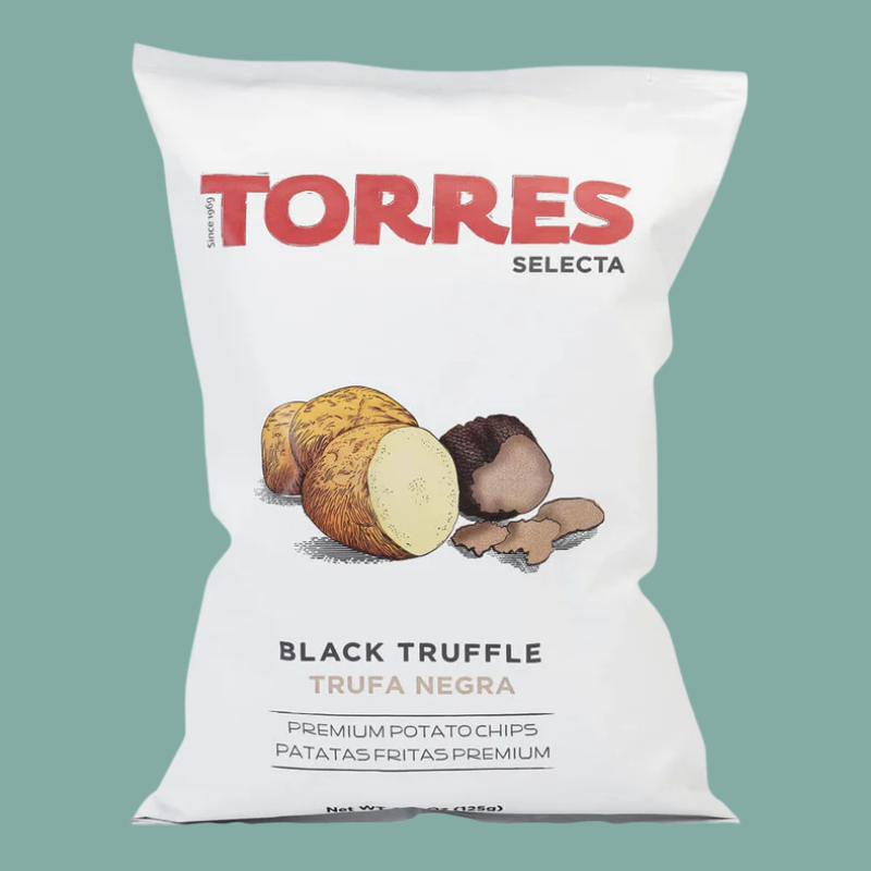 A white bag of TORRES Selecta Black Truffle potato chips, featuring an illustration of black truffle and potato pieces on the front, set against a solid teal background.