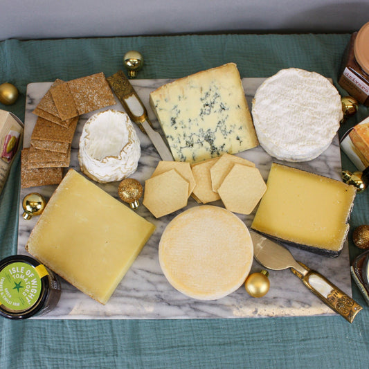 Assorted cheeses with crackers, jam, and honey on a marble board on a teal fabric background.