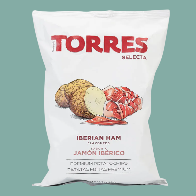 A white bag of Torres Selecta Iberian Ham flavored potato chips, featuring a graphic of a potato and sliced ham on the front, set against a solid teal background.