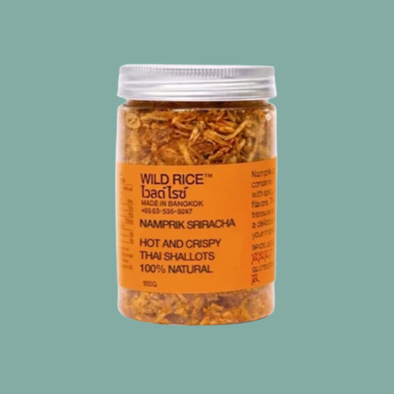 A clear plastic jar of Wild Rice Namprik Sriracha hot and crispy Thai shallots, filled with shredded orange-brown spices, set against a solid teal background.