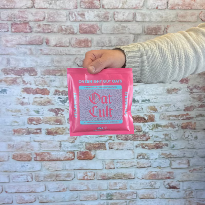 Person holding strawberry Oat Cult in front of a brick-patterned backdrop