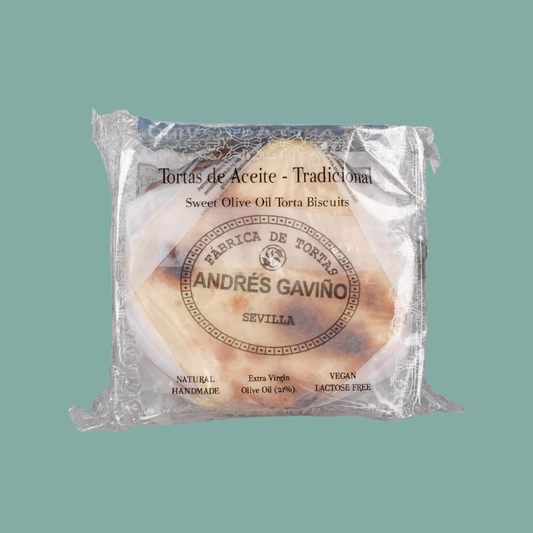 A packaged round sweet olive oil torta biscuit from Andrés Gavino, Seville, wrapped in clear plastic with a printed paper label. The label reads 'Tortas de Aceite - Tradicional' and 'Sweet Olive Oil Torta Biscuits' with the brand name 'ANDRÉS GAVINO'.