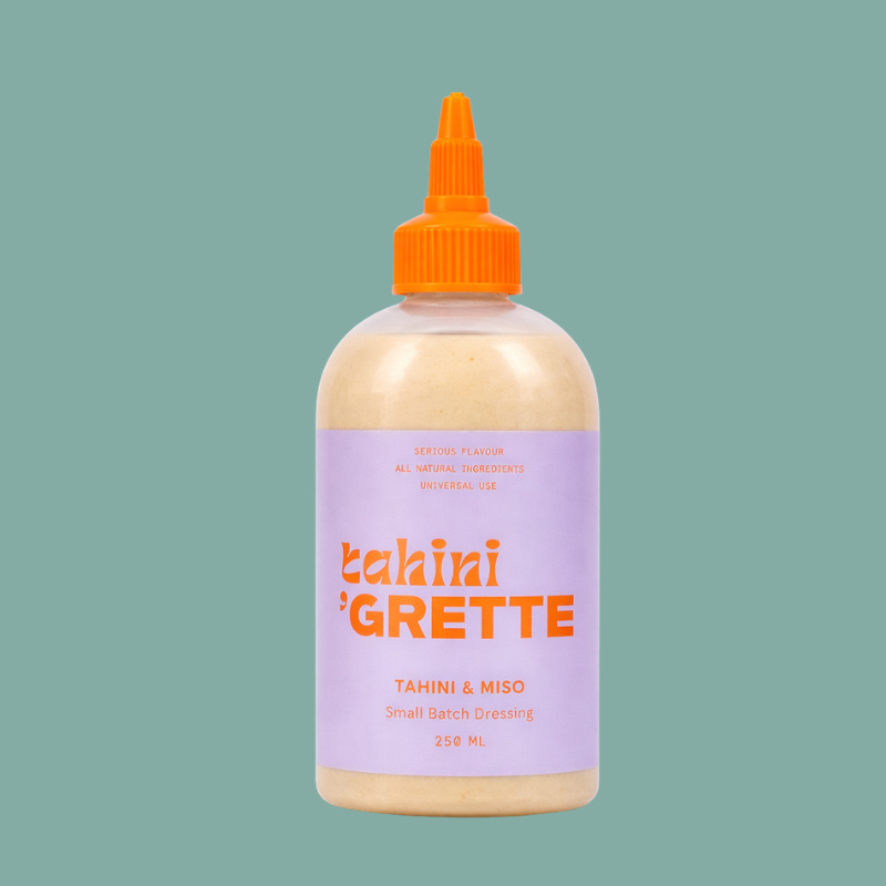 Bottle of tahini Grette dressing with a purple label and orange cap on a green background